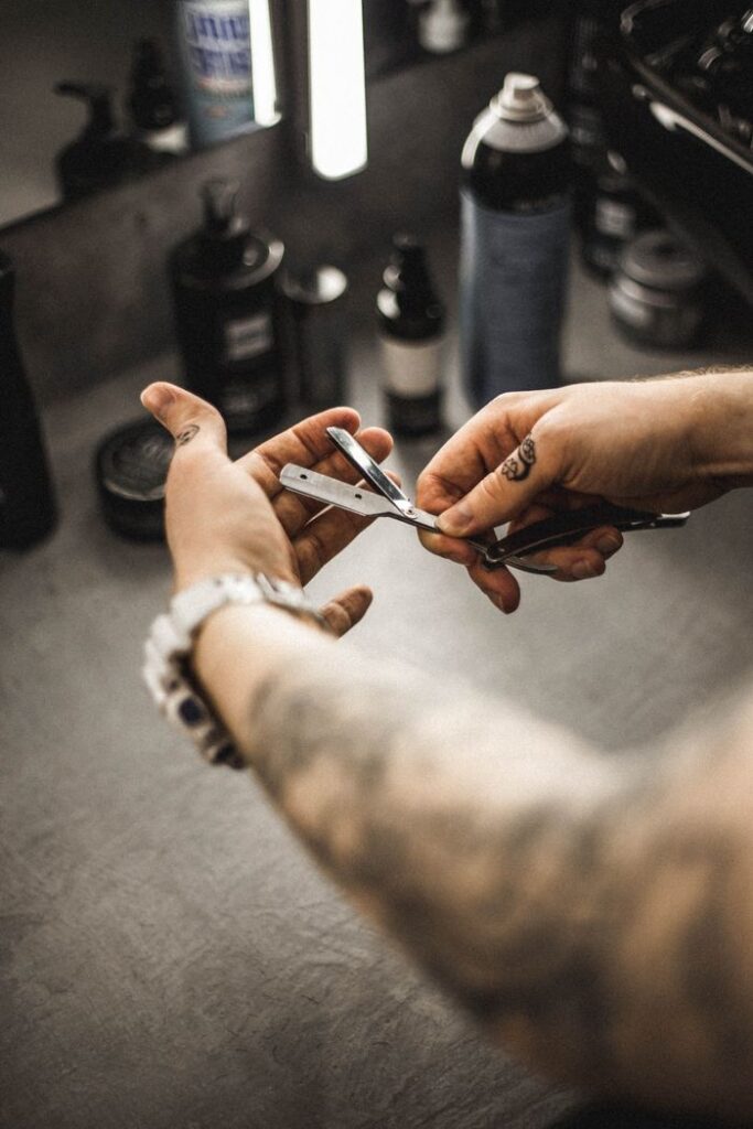 Close-up of a tattooed hand holding a straight razor in a barber shop setting.